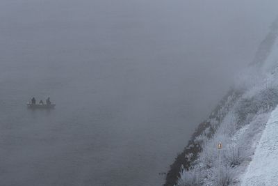 Drei Angler im Boot auf Weser, greuer Wintertag, orangefarbene Uferleuchten